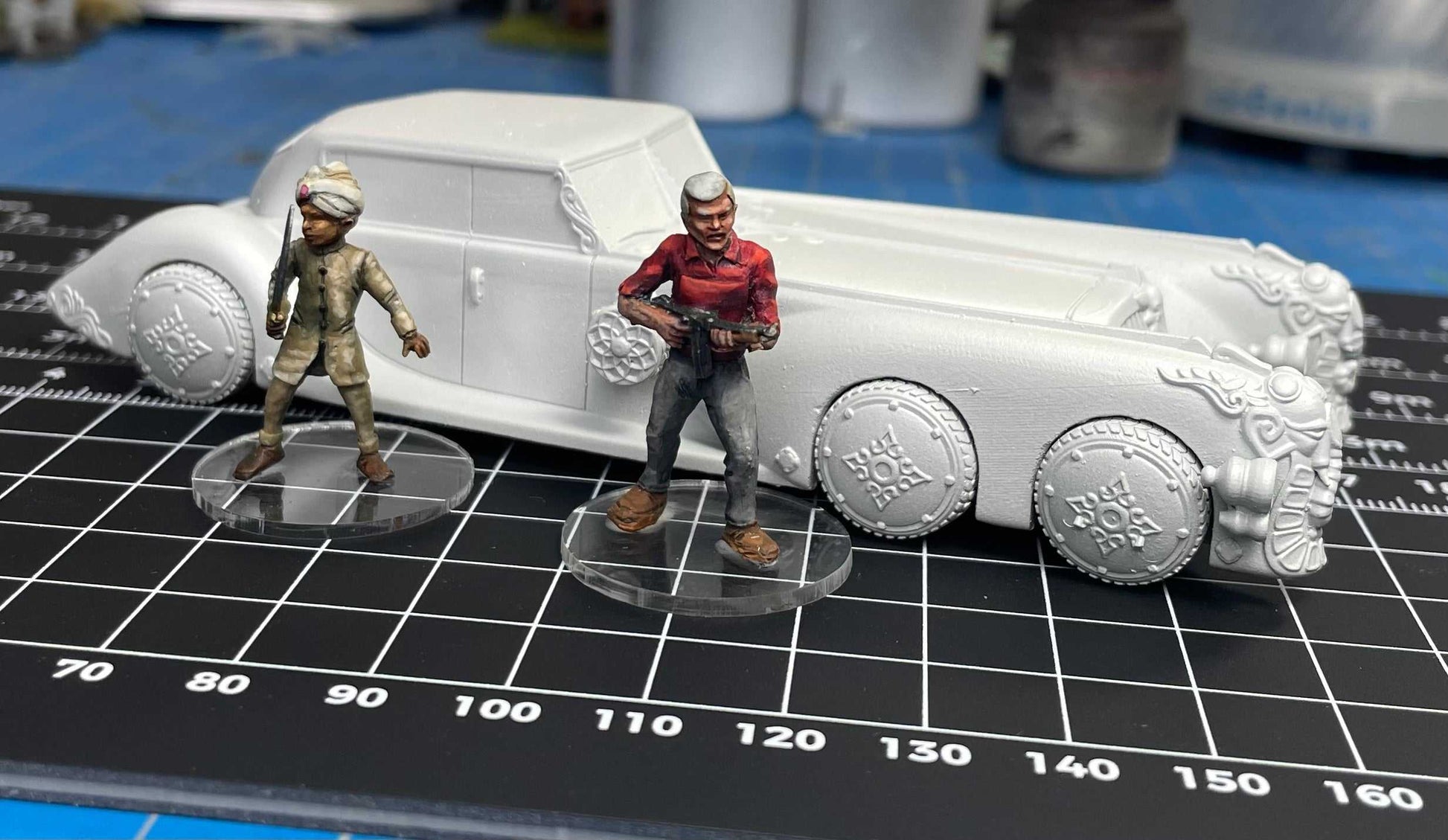 28mm scale resin 3D printed extraordinary car model with two detailed miniature figures on a cutting mat.