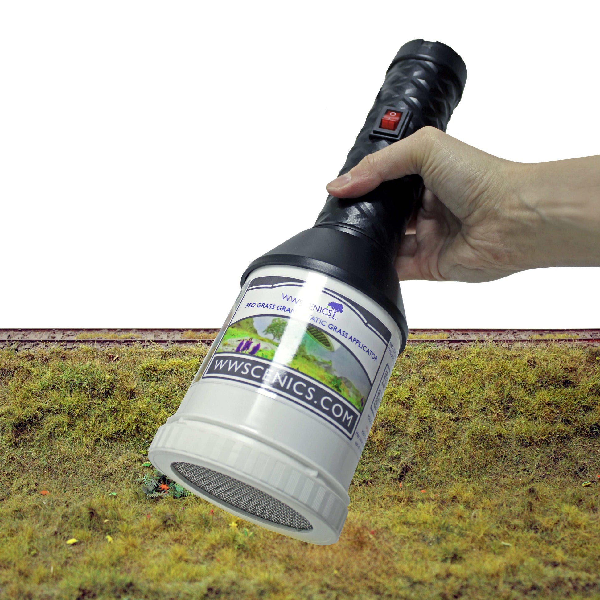 WWScenics Pro Grass Grand Static Grass Applicator held over a textured model grass surface for realistic 3D grass effect