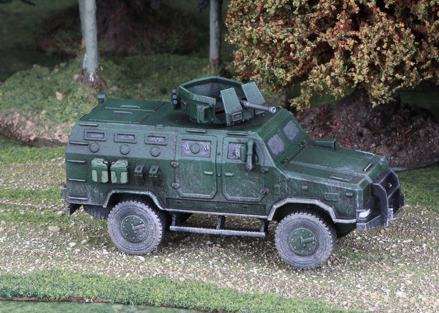 15mm scale model of Ukrainian Kozak armored vehicle in green, detailed and weathered, displayed outdoors on terrain with trees and bushes background