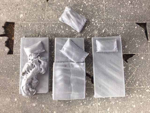 Set of three 28mm modern sleeping mats and pillows modeled after Syrian rooftop mats on a speckled surface