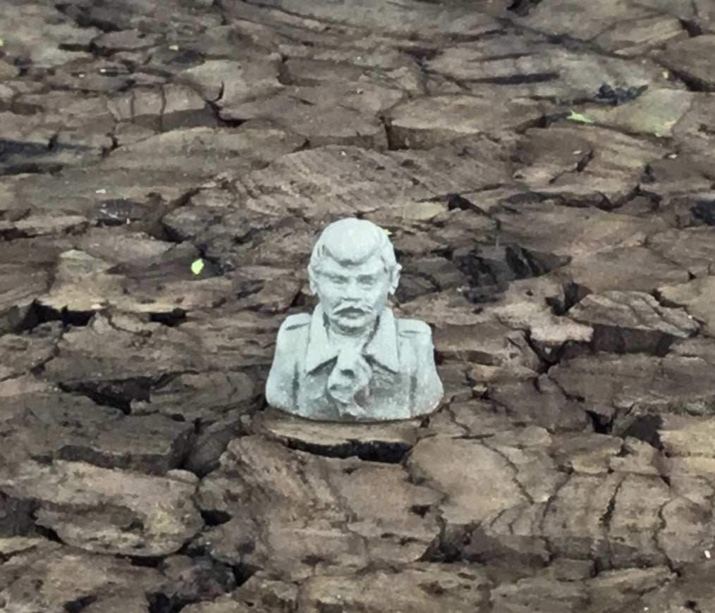 28mm gray bust statue on cracked dry ground resembling a stern man with mustache and jacket