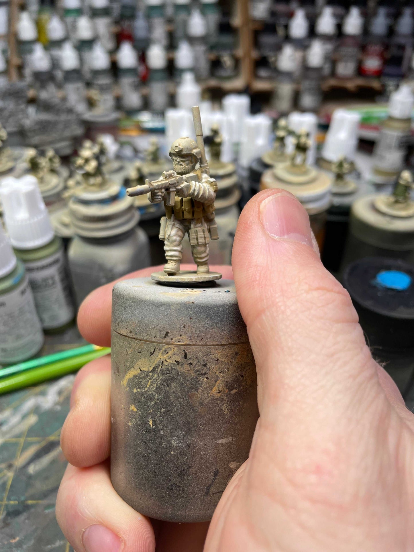 28mm Modern SEALs resin miniature figure holding a rifle, unpainted, on a workbench with painting supplies in the background